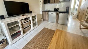Cocina compacta equipada con microondas, estufa y lavavajillas. Un televisor de pantalla plana está instalado sobre un gabinete blanco con espacio de almacenamiento.