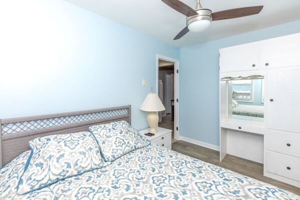 Une chambre à coucher comprenant un lit, une table de chevet, une lampe, un ventilateur de plafond et une armoire.