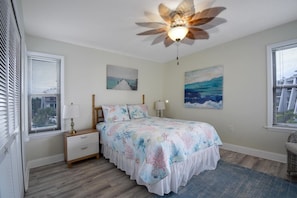 Quarto com cama, mesas de cabeceira, ventilador de teto e obras de arte nas paredes.
