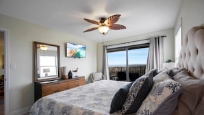 A bedroom with a large bed, a ceiling fan, a view of the ocean, and a balcony. - Oceans Joy (St. Augustine Beach)