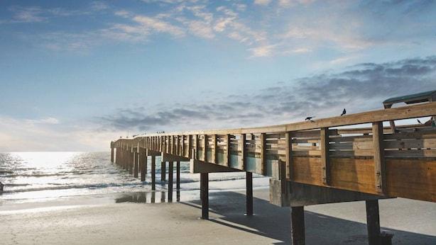 A wooden pier extending into the water with a clear sky above. - Oceans Joy (St. Augustine Beach)