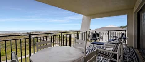 Un balcón con mesa y sillas, vista a la playa y cielo despejado.