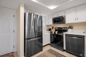A modern kitchen with stainless steel appliances, white cabinetry, and a patterned rug.