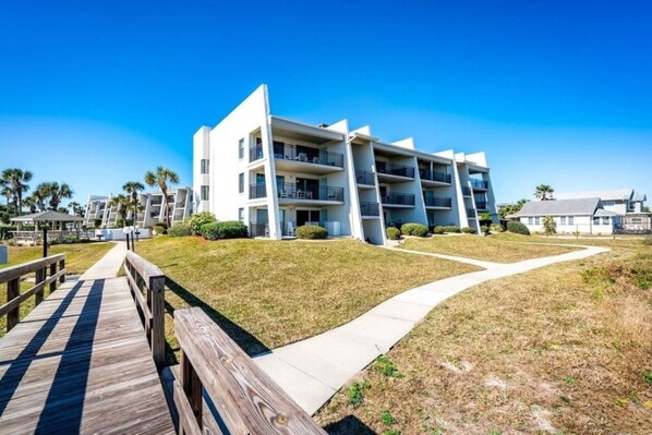 A modern multi-story building with balconies, a wooden boardwalk, and a clear sky.