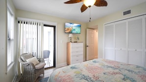 A bedroom with a bed, a chair, a dresser, a television, and a closet. - Oceans Joy (St. Augustine Beach)