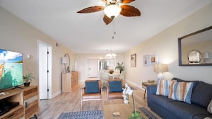 A living room with a television, a ceiling fan, a sofa, and a coffee table. - Oceans Joy (St. Augustine Beach)