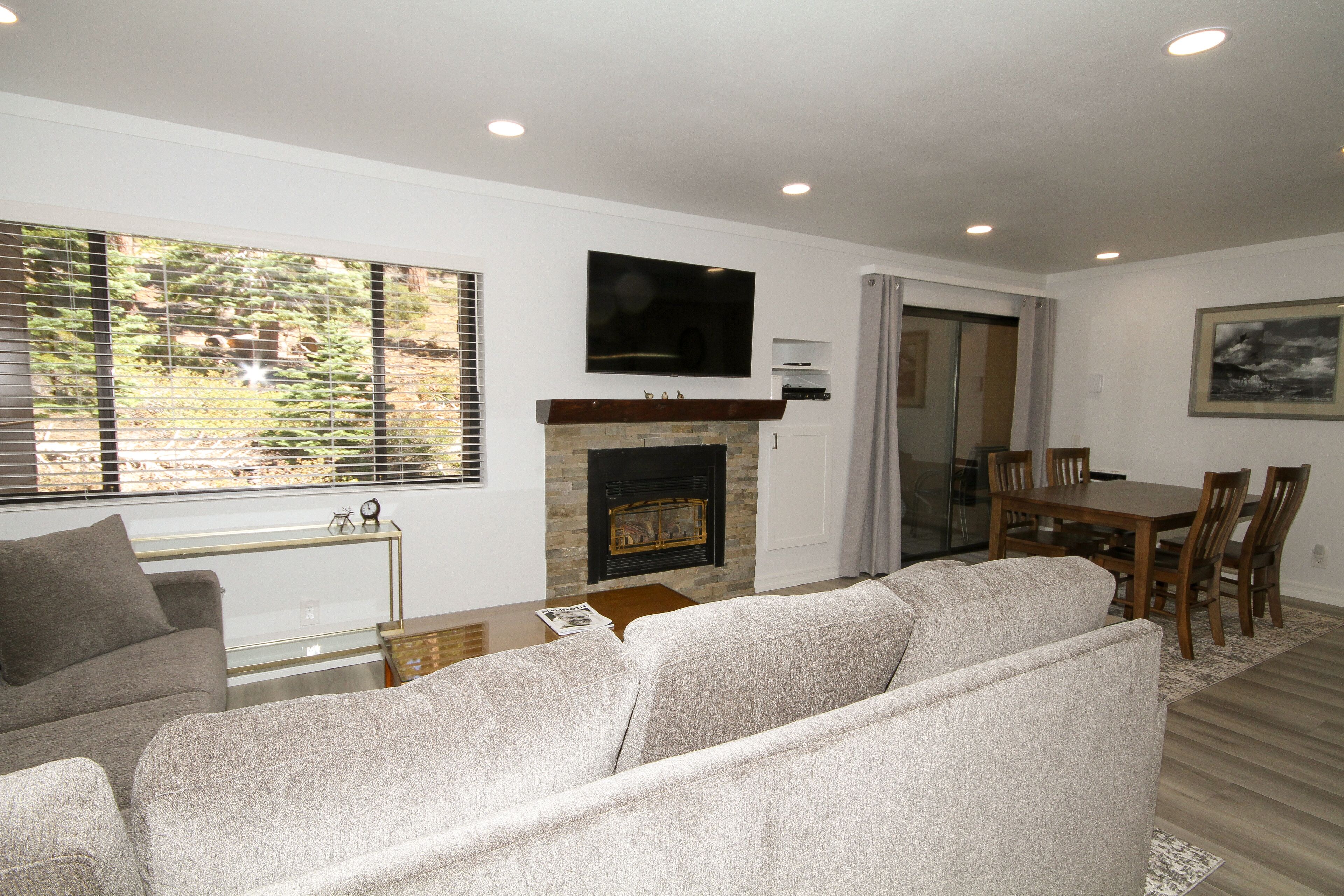 A living room with a fireplace, a television mounted above it, a dining area with a table and chairs, and a sofa.
