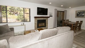 A living room with a fireplace, a television mounted above it, a dining area with a table and chairs, and a sofa. - Mammoth Ski & Racquet Club #127 (Mammoth Lakes)