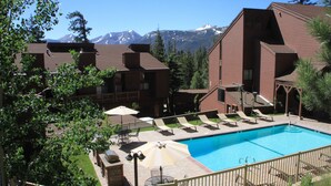 A pool area with lounge chairs and umbrellas, surrounded by buildings with a mountain backdrop. - Mammoth Ski & Racquet Club #127 (Mammoth Lakes)