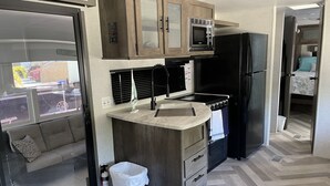 A compact kitchen with a microwave, stove, and refrigerator, a small trash bin, and a window with blinds. - The place to go when you want to get away! (Key Largo)
