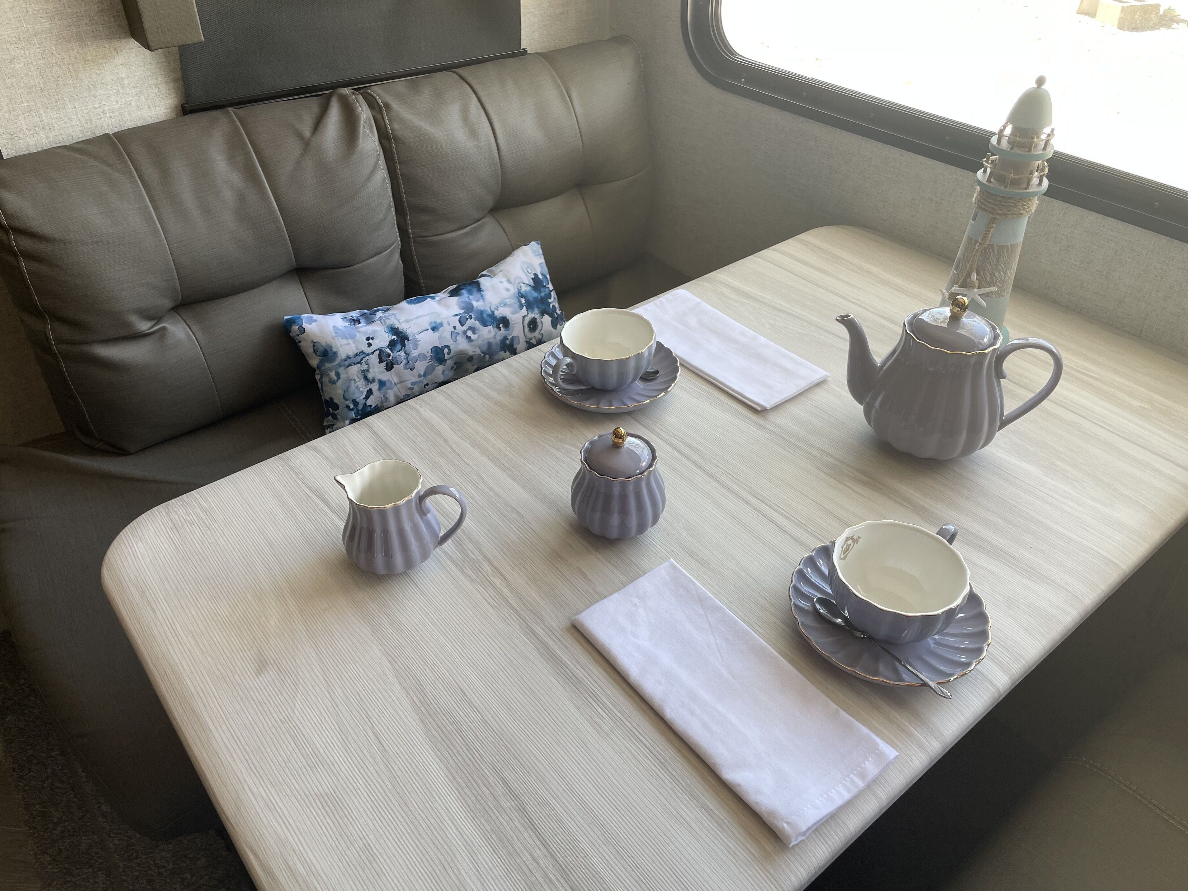 A neatly arranged table with a tea set, a cushion, and a view of the outside.
