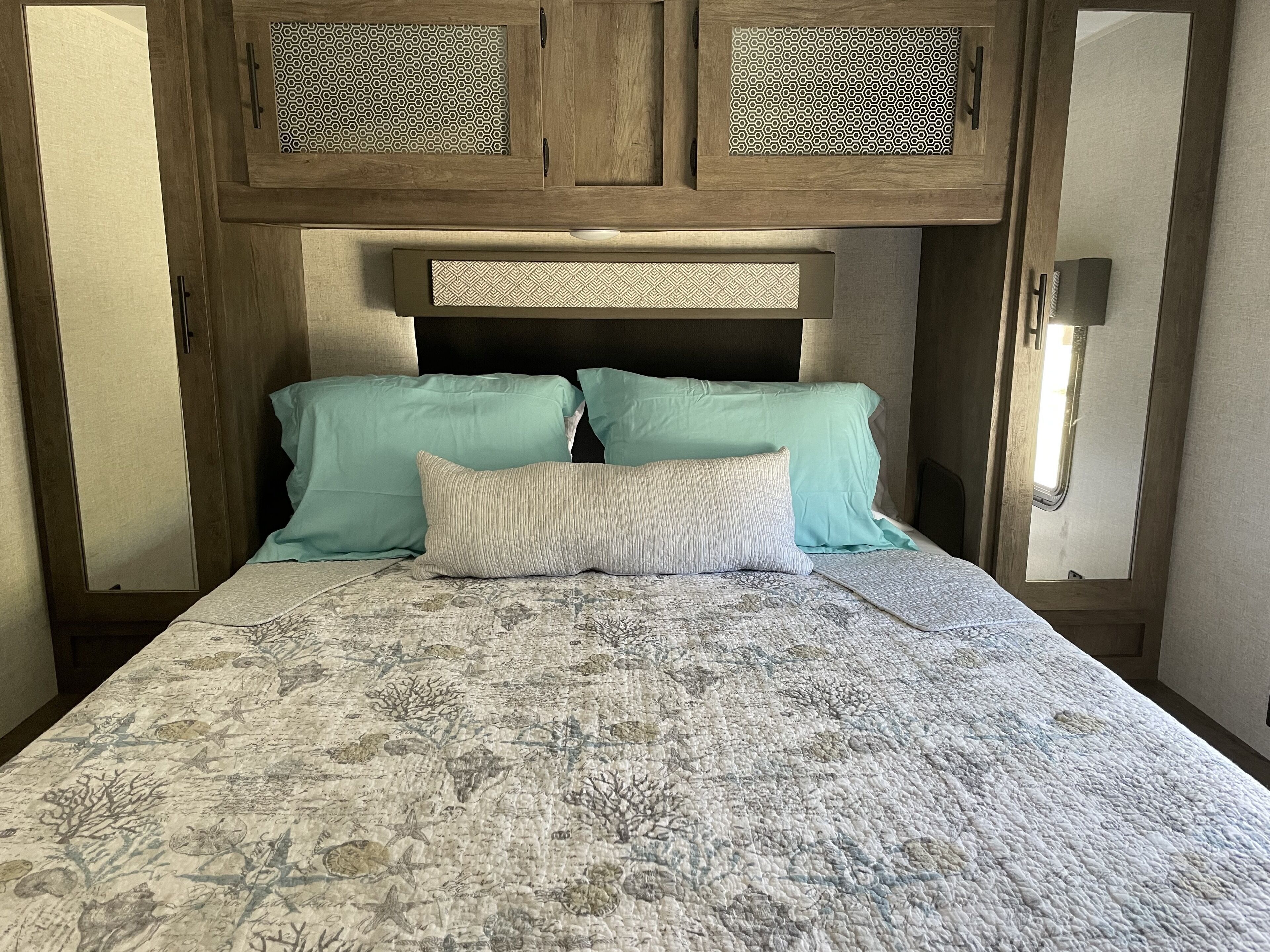 Un lit avec une couvre-lit à motifs, deux oreillers et une tête de lit ornée d’un motif géométrique.