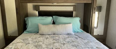 Un lit avec une couvre-lit à motifs, deux oreillers et une tête de lit ornée d’un motif géométrique.