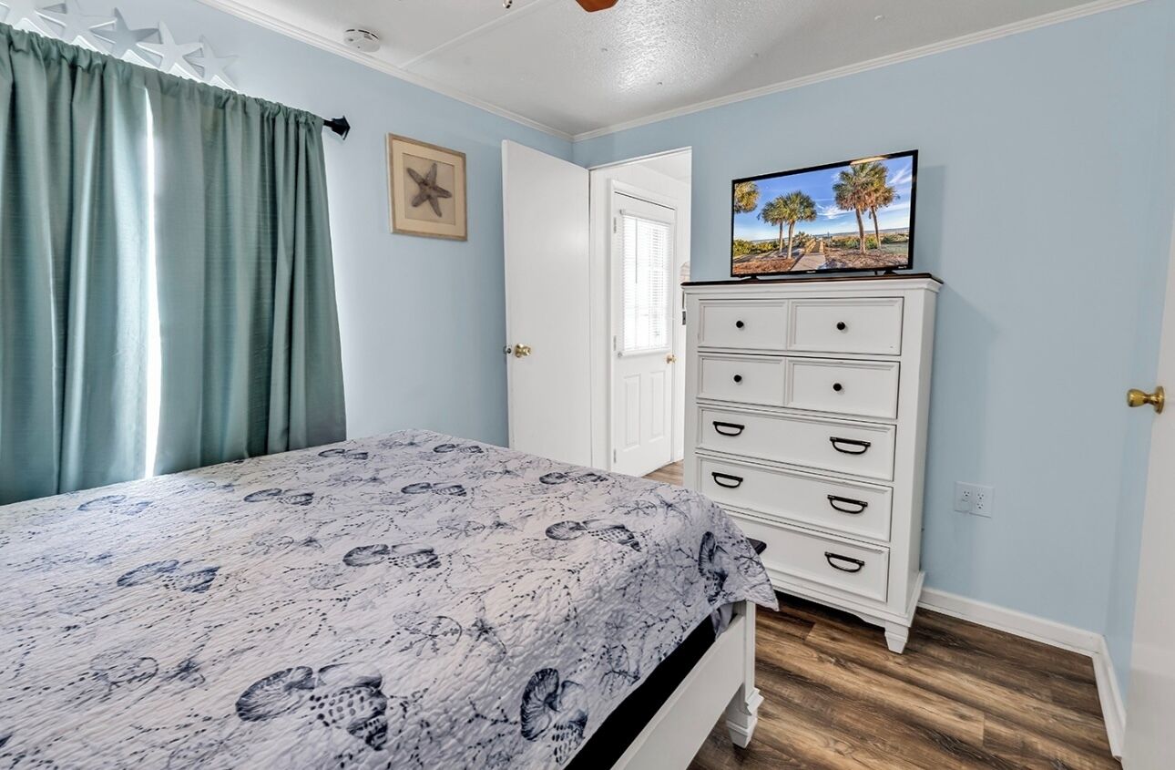 Une chambre à coucher avec un lit, une commode, un téléviseur et une porte.