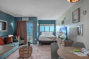 Ein Hotelzimmer mit Bett, einer Couch, einem Esstisch, einem Fernseher und einem Balkon mit VorhÀngen.