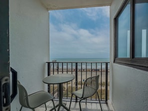 Un balcón con mesa y dos sillas, con vista a una playa y el océano.