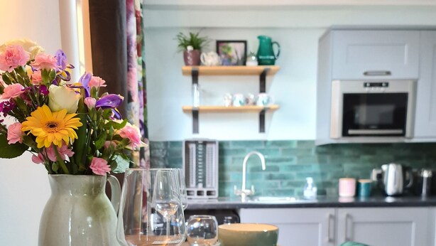 Een eettafel met een bloevas, wijnglazen en borden in een moderne keuken met een groene stoel.