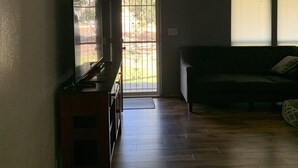 Een woonkamer met een televisie op een houten kast, een bank en een deur die naar buiten leidt.