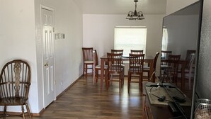 Een ruime eethoek met houten stoelen en een grote eettafel, een televisie op een houten standaard, en een kroonluchter.