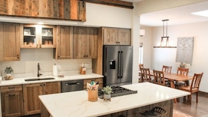 Una cocina con armarios de madera, un refrigerador de acero inoxidable, encimera de mármol y un comedor con sillas y mesa de madera.
