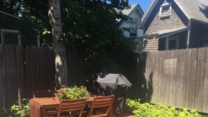 Een terras met een houten tafel en stoelen, omgeven door een betegelde vloer en een houten omheining.