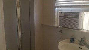 Een badkamer met een douche, wastafel en een raam met zonwering.