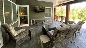 Een overdekt terras met rieten meubilair, een aan de muur bevestigde televisie en een plafondventilator.