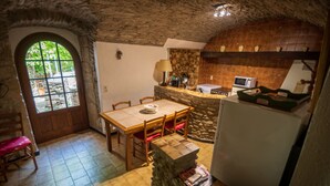 A rustic kitchen with a stone wall, wooden table, and chairs. - 6-person gîte in the large building on the Garidels estate (Gravières)