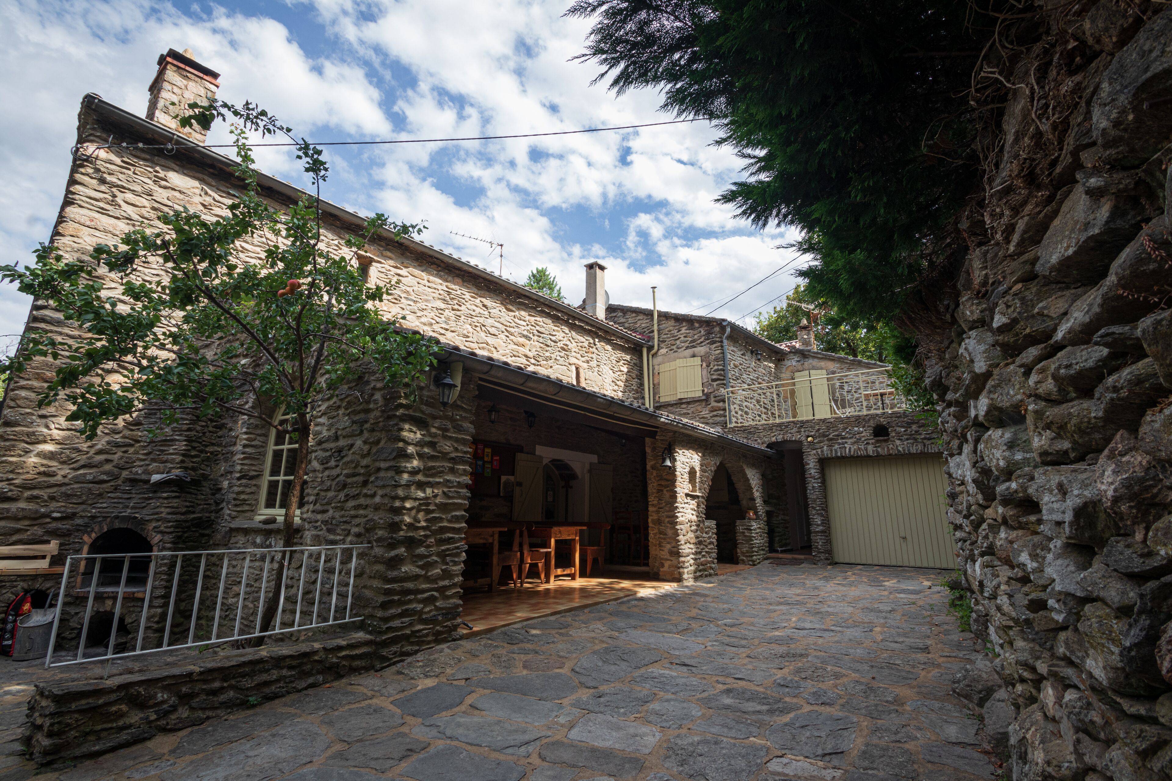 A stone building with a courtyard, a wooden table, and a metal fence.