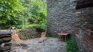 A stone patio with two lounge chairs and a small table, surrounded by greenery and stone walls. - 6-person gîte in the large building on the Garidels estate (Gravières)