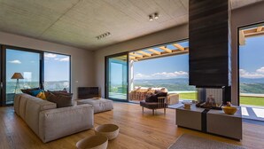 A spacious living room with a large sofa, a coffee table, and a fireplace. There are large windows offering a view of the outdoors. - Villa Grand Horizon with Pool (Pazin)