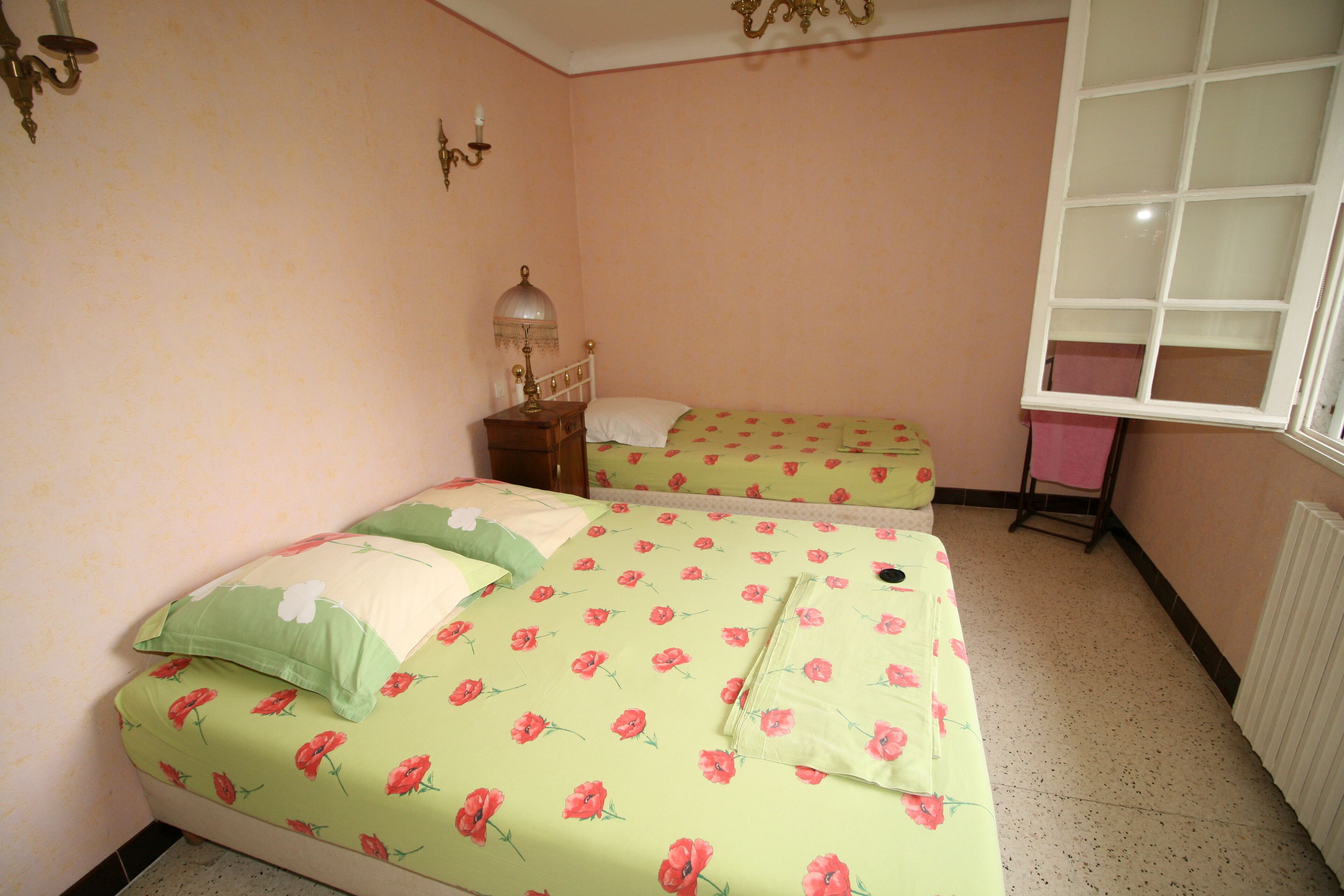 A bedroom with a floral bedspread, a bedside table with a lamp, and a window with a view.