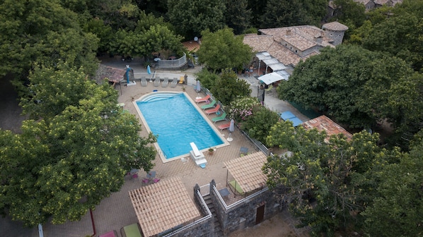 An aerial view of a resort with a swimming pool surrounded by lounge chairs and a stone building.