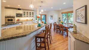 A modern kitchen with granite countertops, white cabinetry, and a central island with bar stools. - Large Home with Ocean Views & Hot Tub! (Santa Barbara)