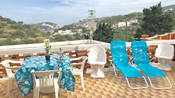 Une terrasse avec une table et des chaises, une vue sur une ville côtière et une antenne parabolique.