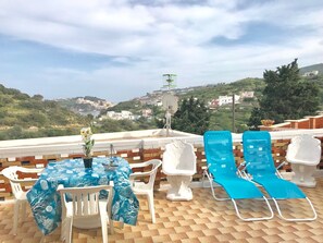 Une terrasse avec une table et des chaises, une vue sur une ville côtière et une antenne parabolique.