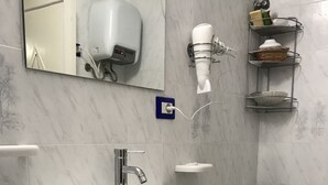 Une salle de bain avec un lavabo blanc, un miroir, un sèche-cheveux et une étagère contenant des articles de toilette.