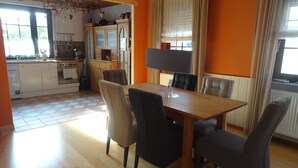 A dining area with a wooden table and chairs, a kitchen in the background, and a window with curtains. - Country house style meets modernity (Mühlheim am Main)