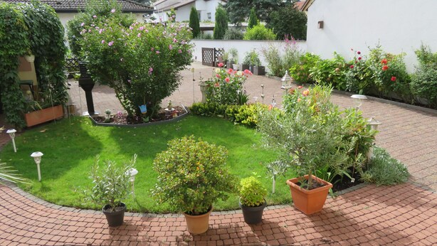 A well-maintained garden with various plants and flowers, a brick pathway, and a white building in the background. - Country house style meets modernity (Mühlheim am Main)