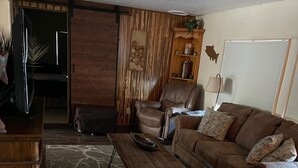 A living room with a brown leather sofa, a wooden coffee table, a patterned rug, and a wooden cabinet.