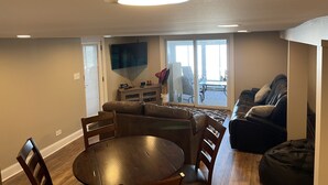A living room with a dining table, chairs, a sofa, and a TV mounted on the wall. - Pet Friendly Huge Lake Front Home with Stunning Views (Round Lake Park)