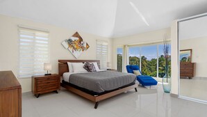 Un dormitorio con cama, mesita de noche, silla, un amplio ventanal y vistas al exterior.