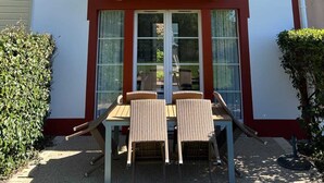 Un edificio de dos pisos con un balcón, un comedor con sillas y una mesa, y un ventanal grande.