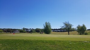 Un campo de golf con club house, árboles y cielo despejado.