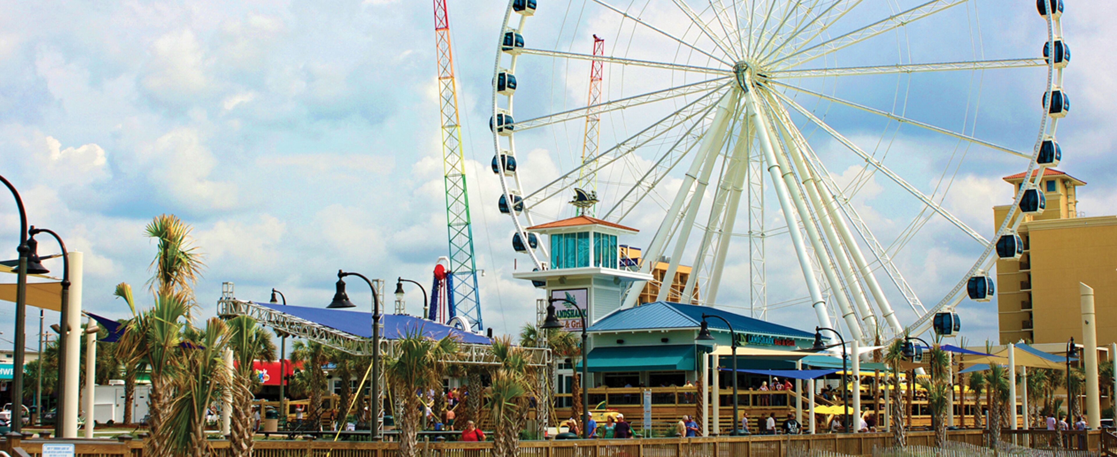 Ein Riesenrad, eine Promenade und ein Gebäude mit einem blauen Dach.