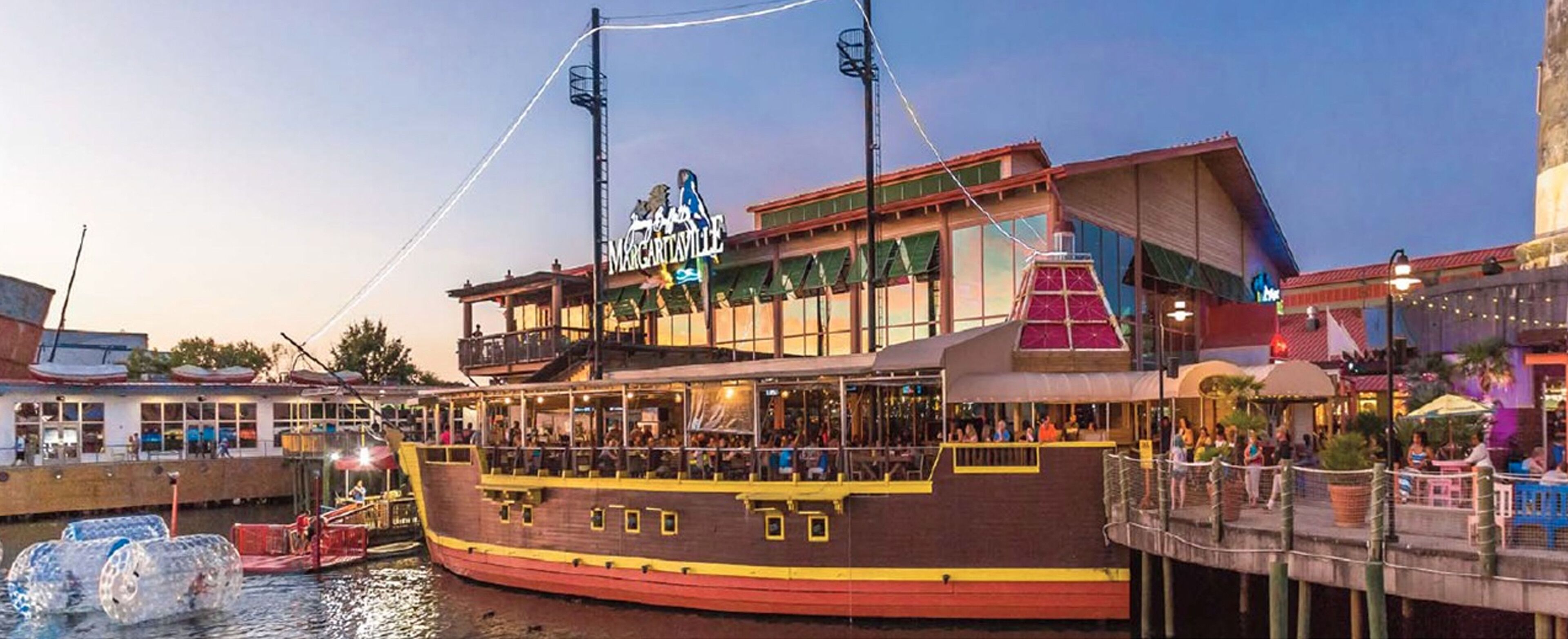 En stor båt med flera däck, där det finns en restaurang på övre däck. Båten ligger förtöjd vid en småbåtshamn, och i närheten finns en byggnad med en skylt som visar texten "MARINELAND".