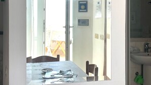A room with a large mirror reflecting a dining area, a door leading outside, and a bathroom with a sink and towel rack. - Conti Holiday Homes - Begonia (Ponza)
