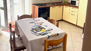 A dining area with a table set for four, a kitchen with yellow cabinets, a microwave, and a gas stove. - Conti Holiday Homes - Begonia (Ponza)