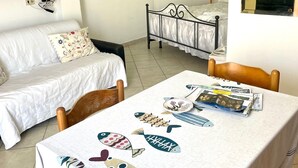 A cozy room with a bed, a dining table with a fish-patterned tablecloth, and a kitchen area visible through an archway. - Conti Holiday Homes - Begonia (Ponza)