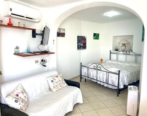 Een slaapkamer met een bed, een bank, een airconditioning en een televisie.
